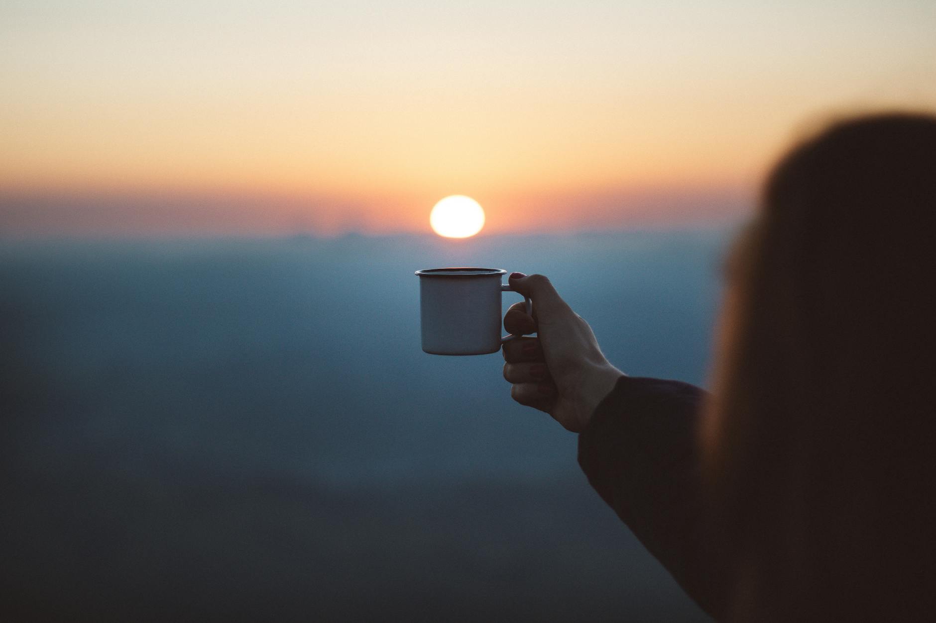 person showing white mug in focus photography - sunrise - welcoming the new day