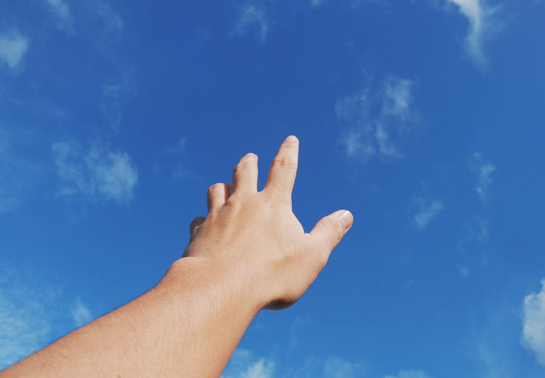 man reaching his hand towards blue sky
