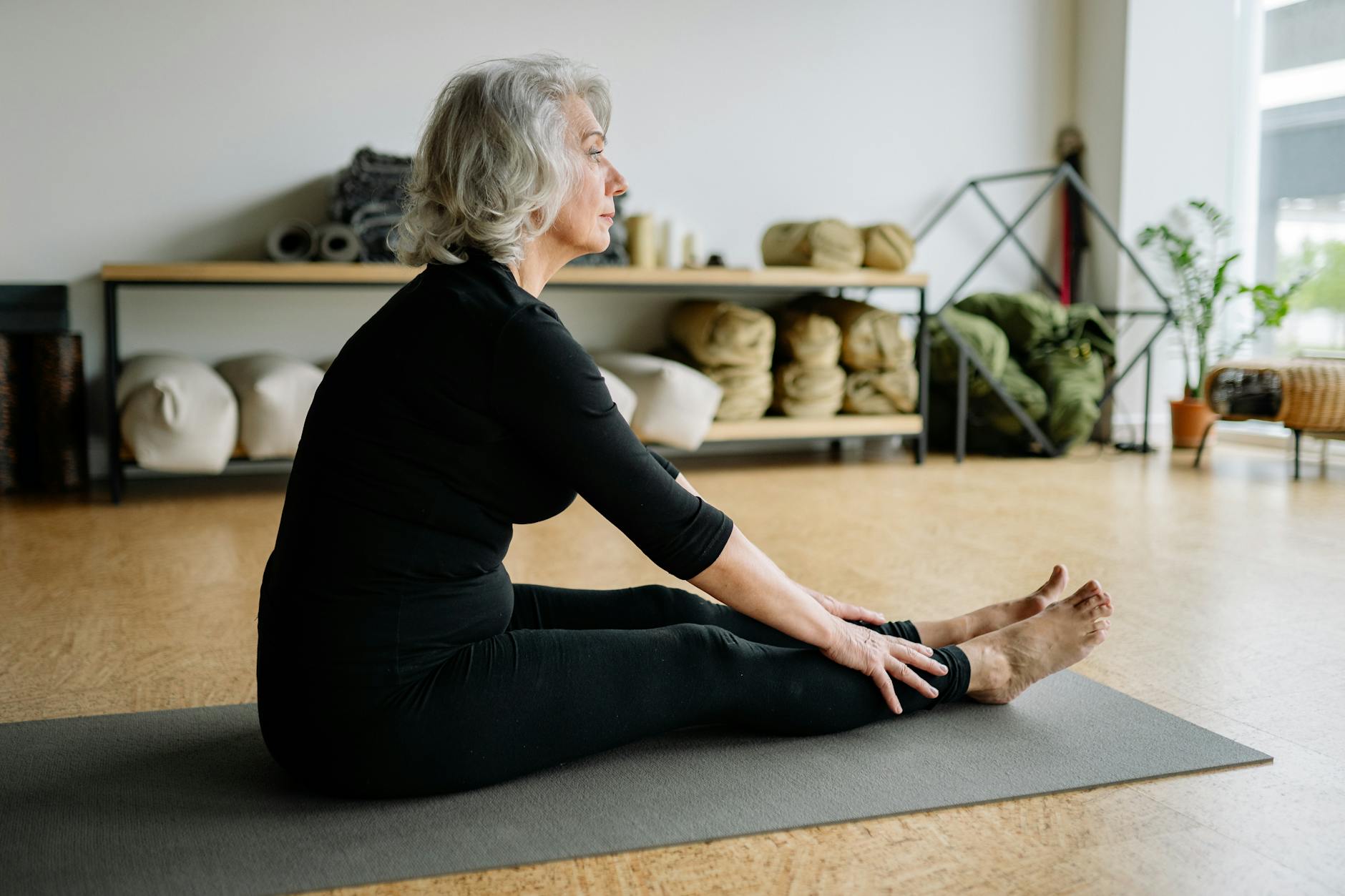 elderly woman in black clothing sitting on yoga mat