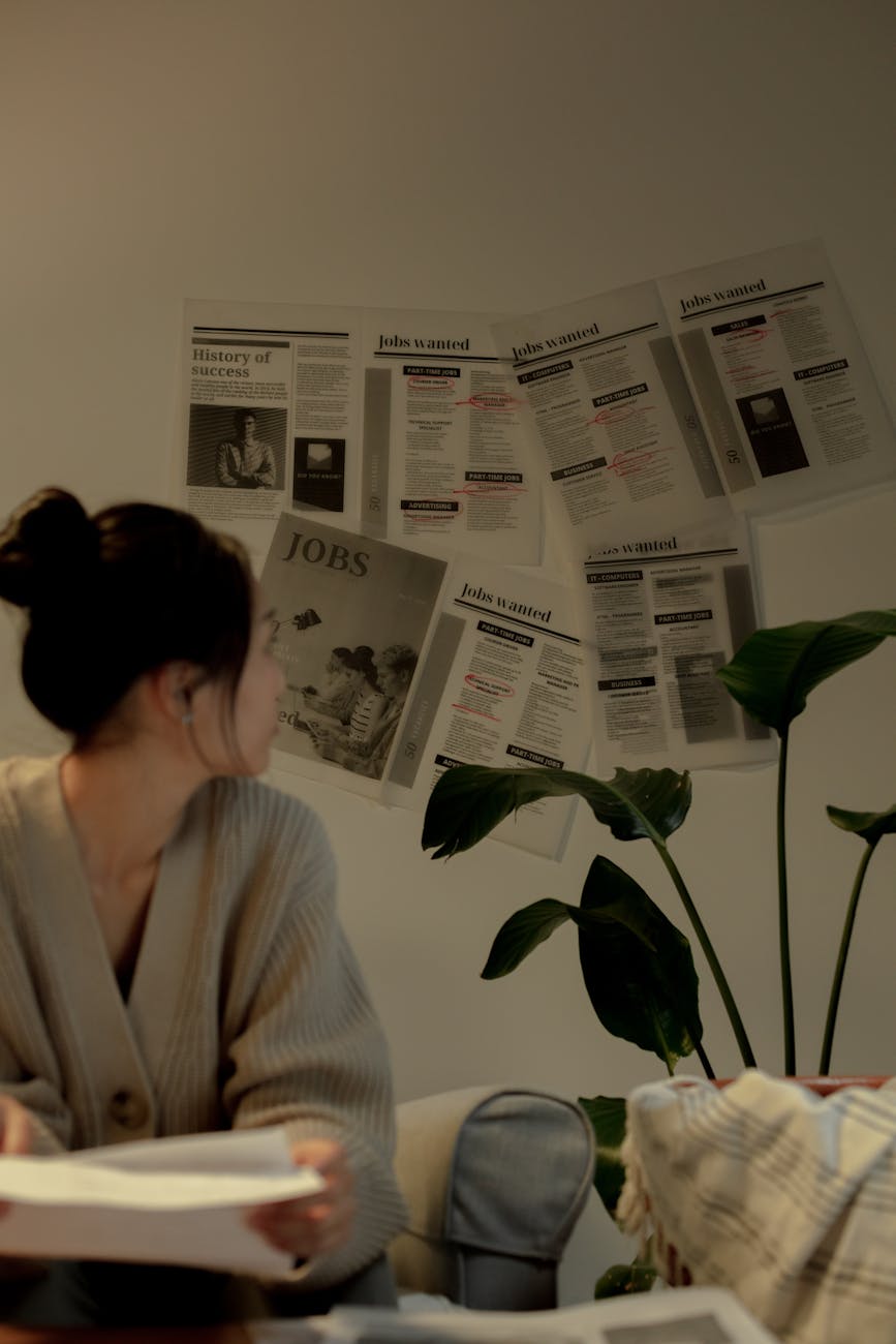 a woman in beige sweater sitting while looking at the newspapers on the wall