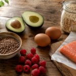 Whole foods that naturally support GLP-1 release, including avocado, eggs, lentils, salmon, raspberries, and oats, arranged on a rustic wood surface.